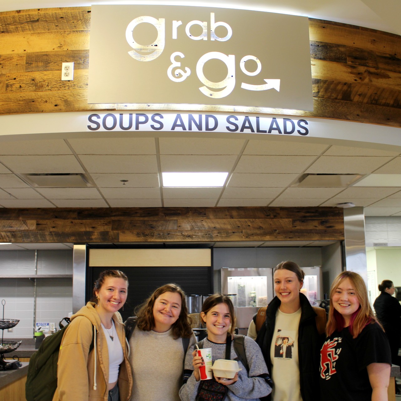A group of friends smiling in the food court near Grab & Go: Soups and Salads