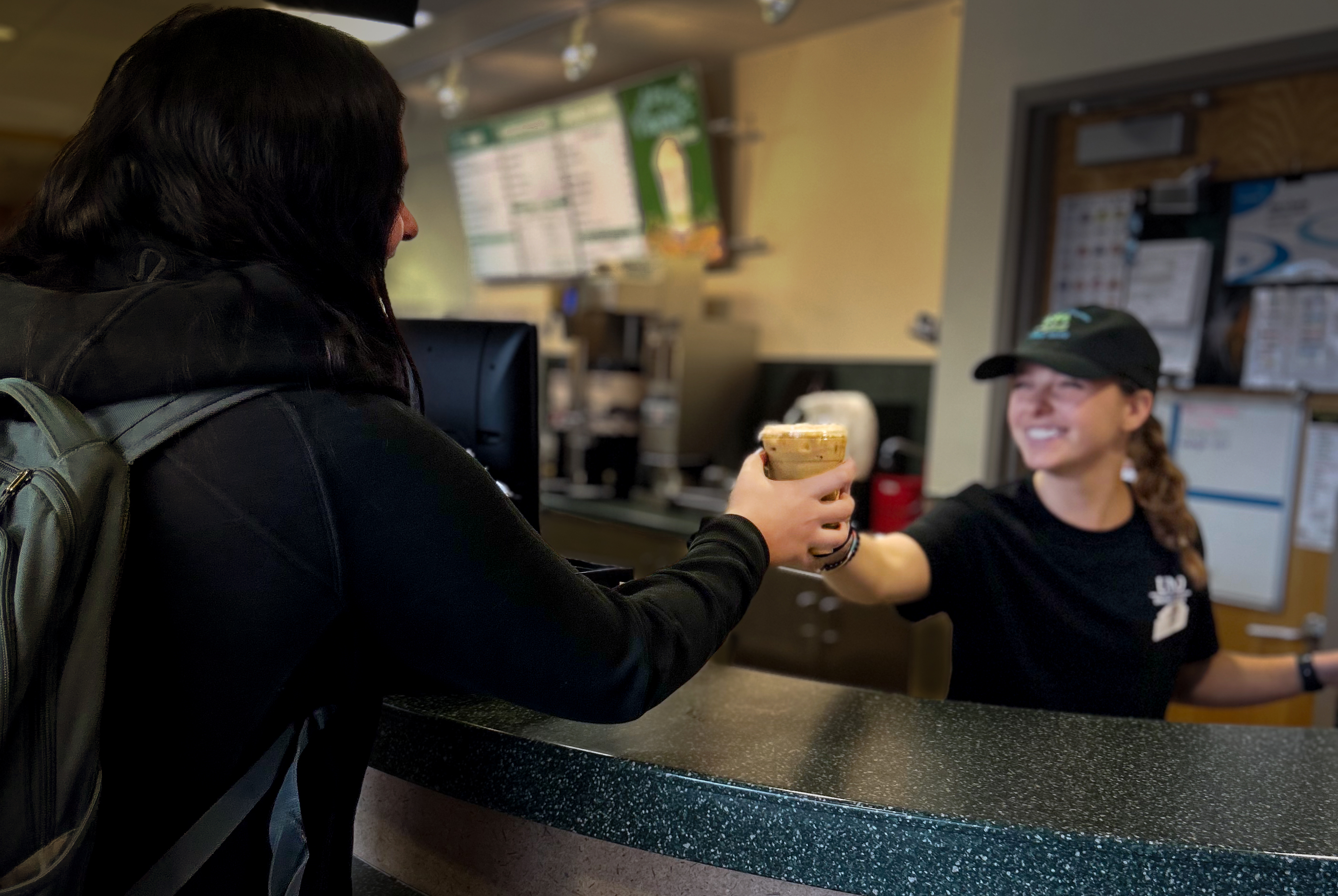Northern Shores Coffee Shop employee hands a guest their coffee order with a smile