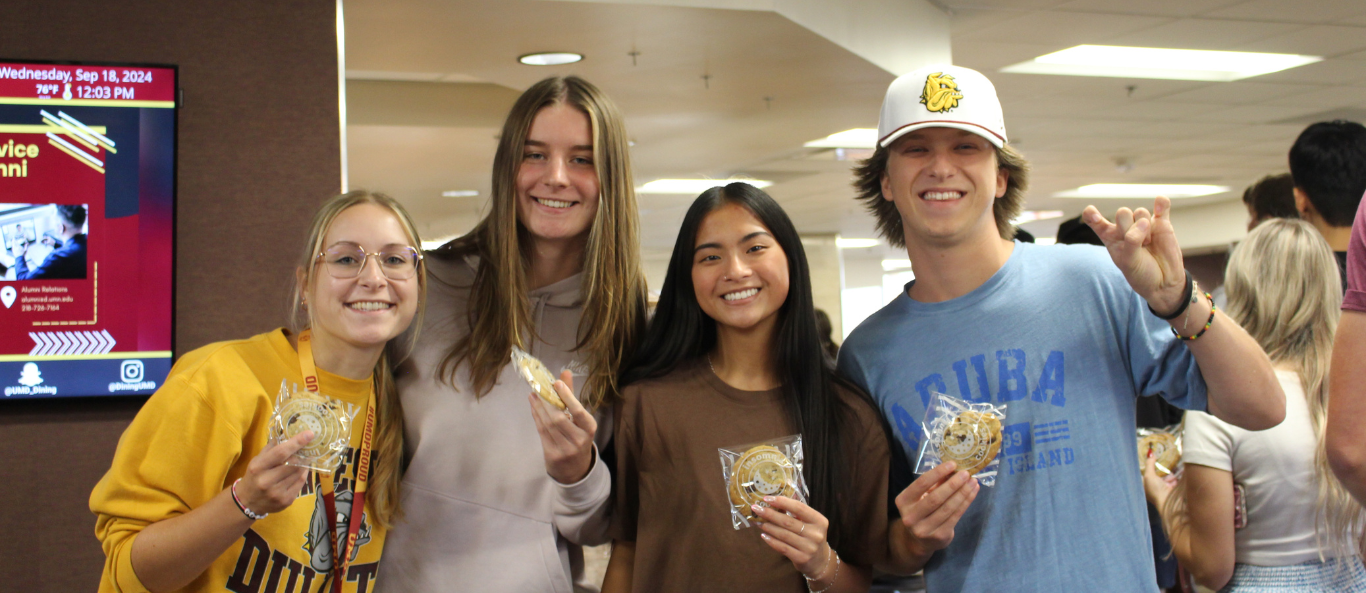  Four students in a Superior Dining hold cookies, smiling at the camera. 
